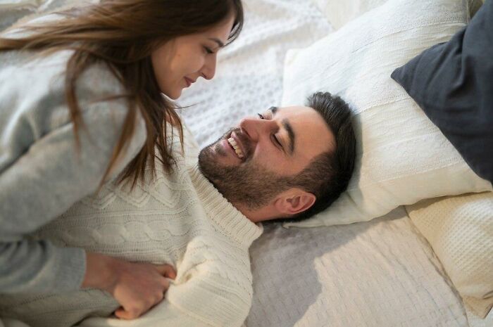 Woman playfully leaning over a smiling man in a cozy setting, capturing a lighthearted moment on their minds.