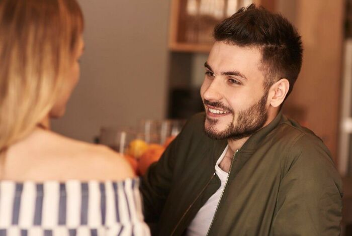 Man in green jacket smiles while talking to a woman, illustrating conversation dynamics between men and women.