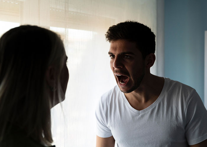 Man in white shirt expressing shock during conversation about partner's comments.