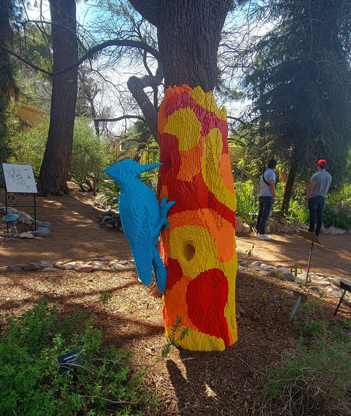 A vibrant LEGO woodpecker sculpture on a colorful tree trunk in a garden, showcasing cool LEGO builds.