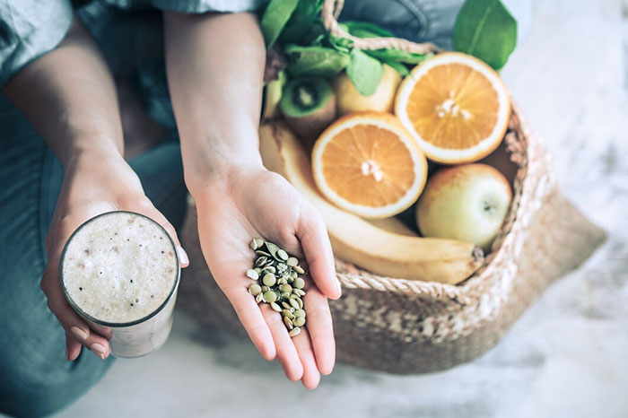 Hand holding seeds alongside a smoothie and fruits, illustrating crazy body life hacks.