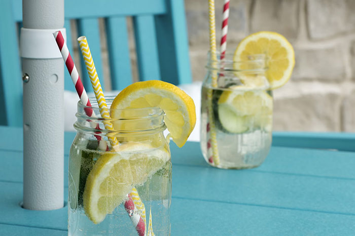 Two mason jars with lemon slices and striped straws on a blue table, showcasing refreshing crazy body life hacks.