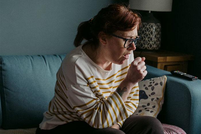 Woman coughing on a blue couch, trying a crazy body life hack for relief.