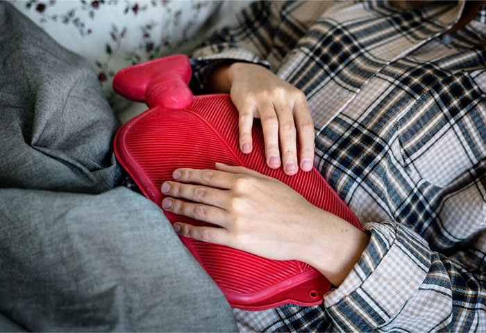 Person using a hot water bottle on abdomen, showcasing a life hack for comfort and relief.