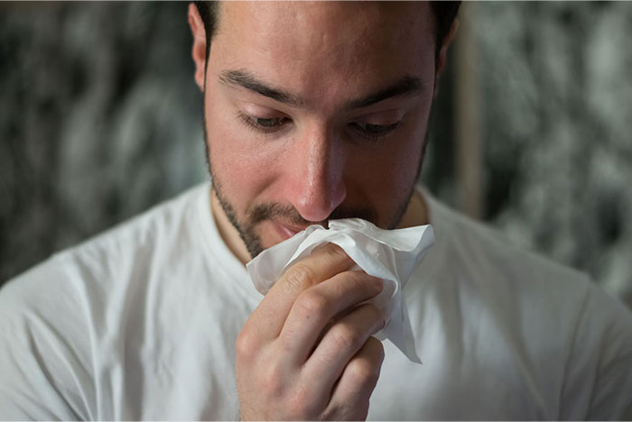 Man using a tissue, exemplifying crazy body life hacks for seasonal allergies.