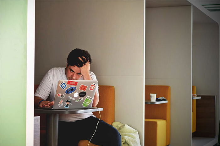 Man using laptop covered in tech stickers, showcasing crazy body life hacks theme in a casual lounge setting.