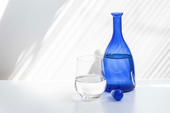 Blue glass bottle and clear glass half full of water, showcasing body life hacks.