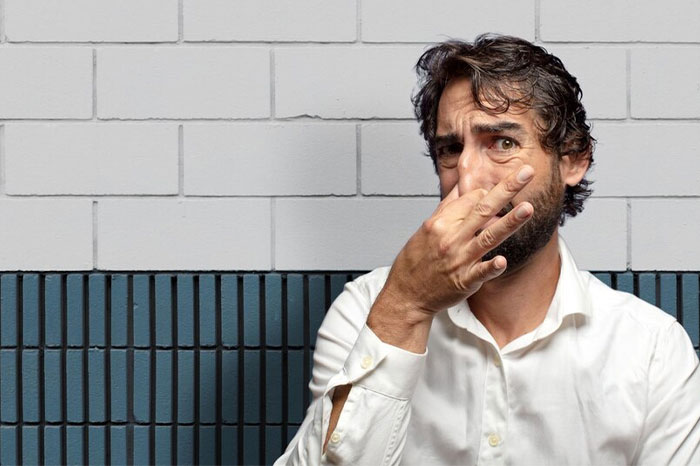 Man in white shirt demonstrating quirky body hack against a tiled wall.