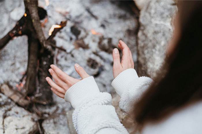 Hands warming by a fire, demonstrating a practical body hack for staying warm in cold environments.