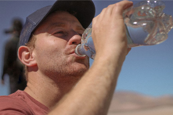 Man wearing a cap drinks water outdoors, showcasing crazy body life hacks for staying hydrated.