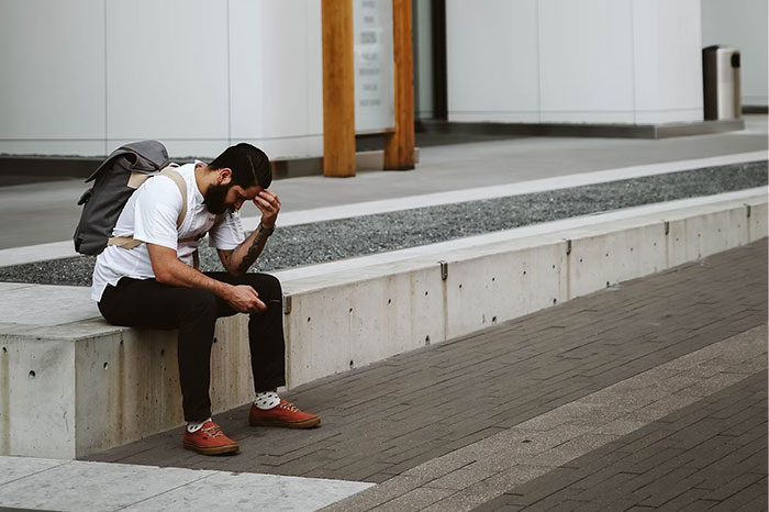 Man sitting on a concrete bench, wearing a backpack, exploring crazy body life hacks on his smartphone.