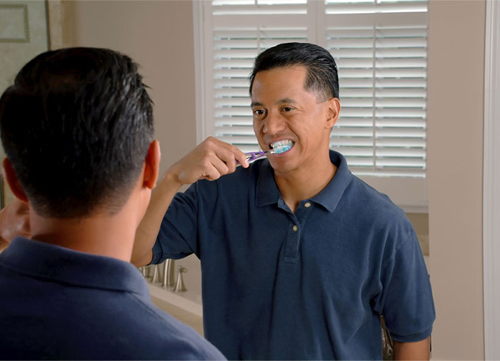 Man brushing teeth in front of a mirror, showcasing crazy body life hacks in a blue shirt and bathroom setting.