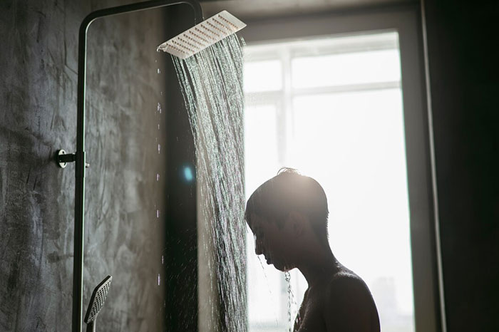 Person using a shower with water streaming down, backlit by sunlight. Crazy body life hacks concept.