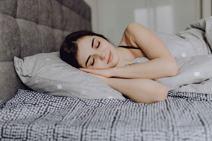 Woman peacefully sleeping in bed, illustrating crazy body life hacks for better rest.