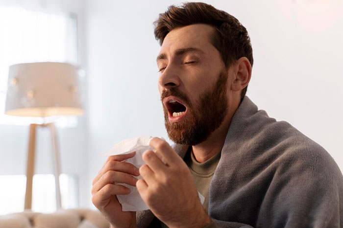 Man sneezing with a tissue, demonstrating a crazy body life hack for relieving congestion.