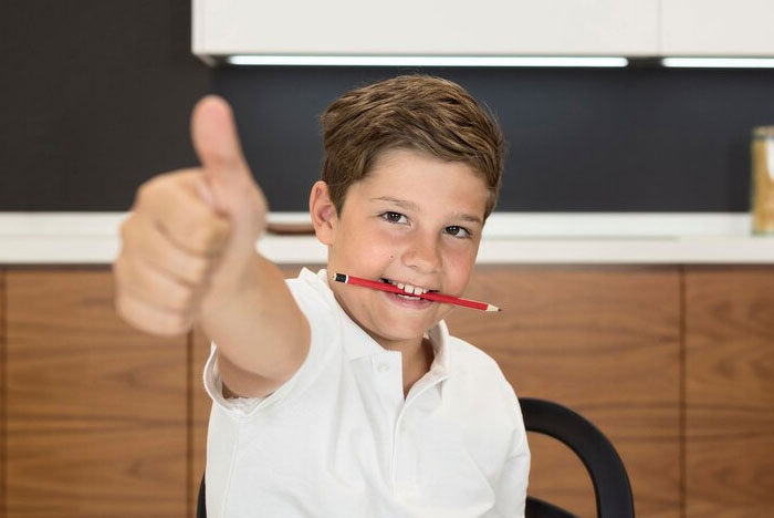 Child demonstrates a life hack by holding a pencil with teeth and giving a thumbs up, showcasing crazy body life hacks.