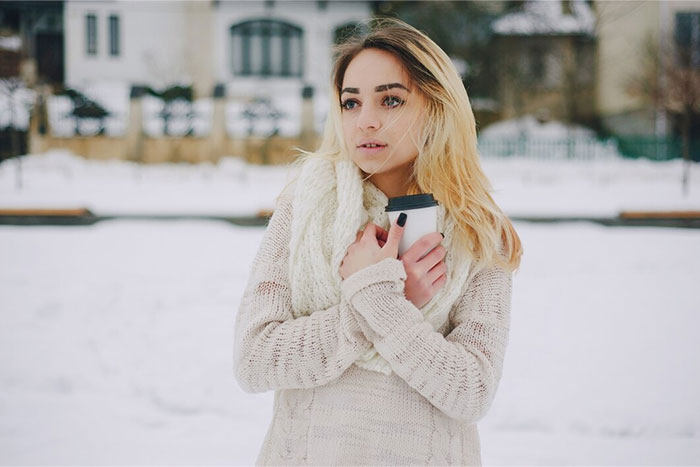 Woman outside in the snow, embracing a cup for warmth, demonstrating a crazy body life hack.