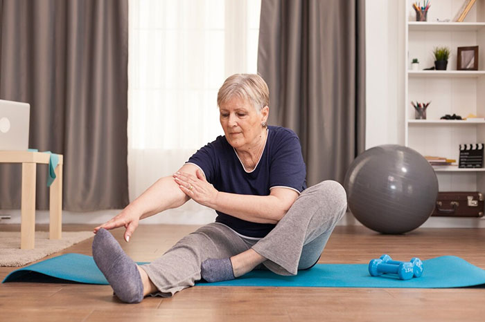 Older woman practicing body life hacks with stretching exercises at home on a yoga mat.