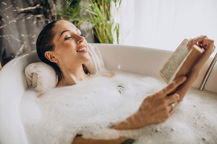 Woman reading in a bubble bath, relaxing with crazy body life hacks for wellness.