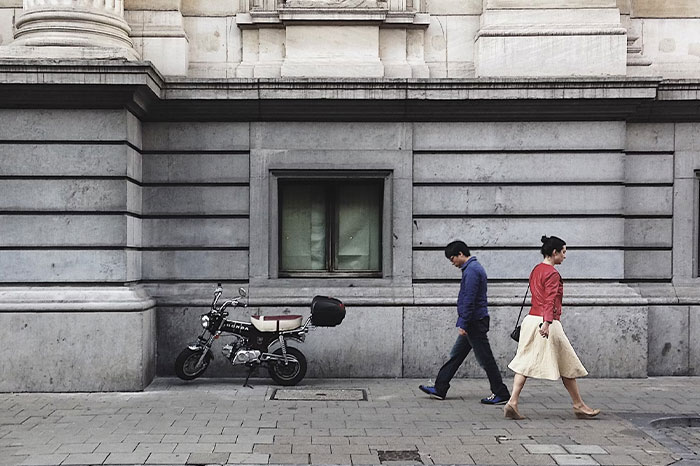 People walking past a parked motorcycle by a building, illustrating urban life hacks.