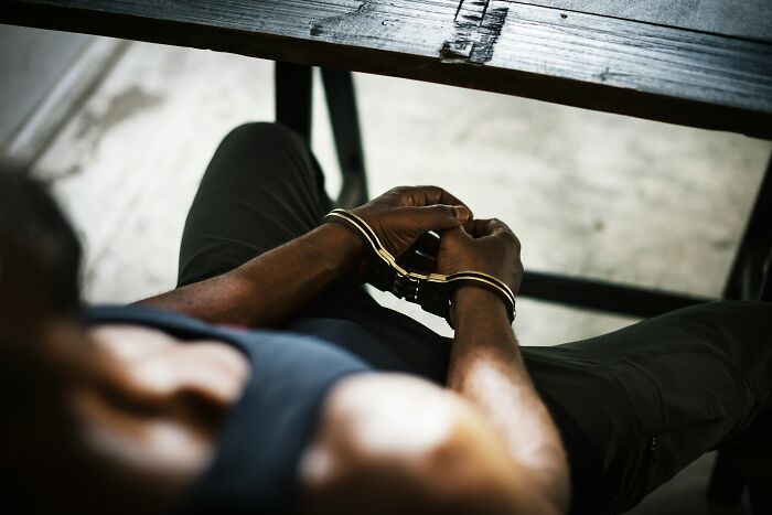 Person in handcuffs sitting at a table, hands bound, representing secrets kept from loved ones.