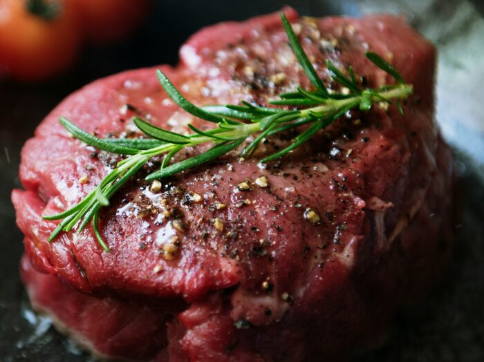 Close-up of seasoned raw steak garnished with rosemary, highlighting an insane coincidence in culinary presentation.