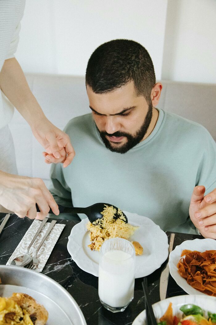 Man sitting at a table with a worried expression, looking at a plate of food being served, highlighting secrets kept from loved ones.