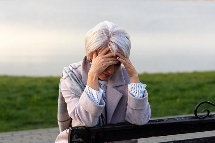 Stressed mom sitting on a bench, head in hands, coping with teen parenting challenges related to ADHD symptoms.