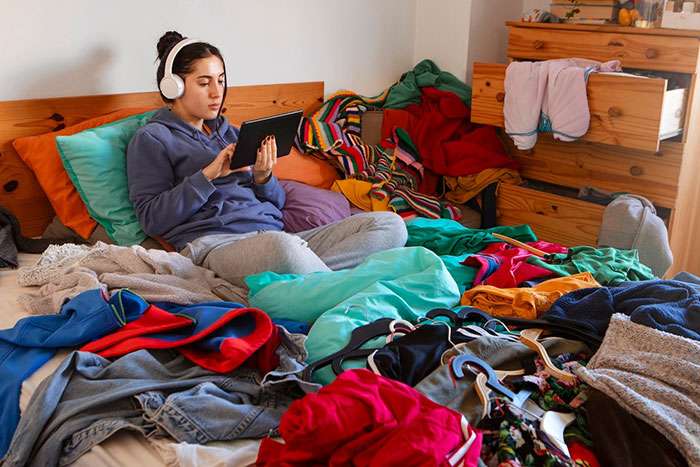 Teen in a messy room, wearing headphones and using a tablet, depicting struggles with potential ADHD symptoms.