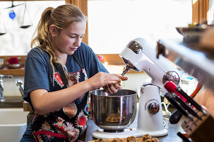 Teen girl baking Christmas cookies in kitchen using a stand mixer.