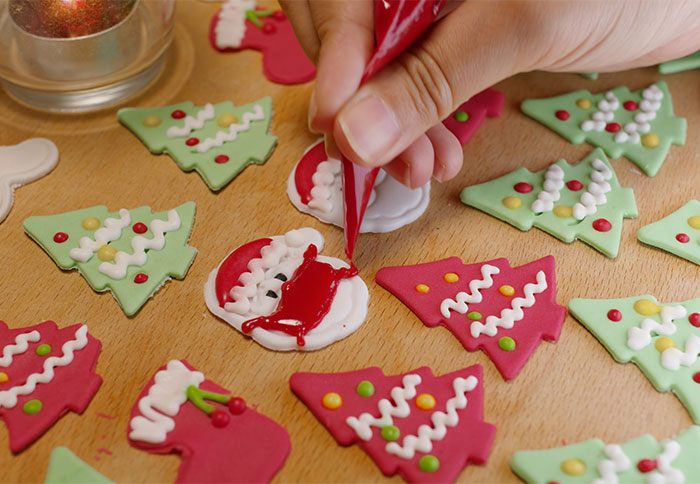 Hand decorating Christmas cookies with icing on a wooden table, featuring festive tree and Santa designs.