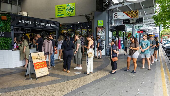 People lined up outside a cafe, possibly judging others discretely while waiting in line.