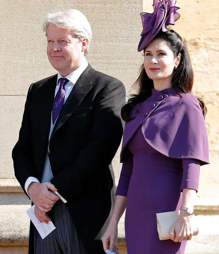 A man in a suit and a woman in a purple outfit with a matching hat, standing outdoors at an event.