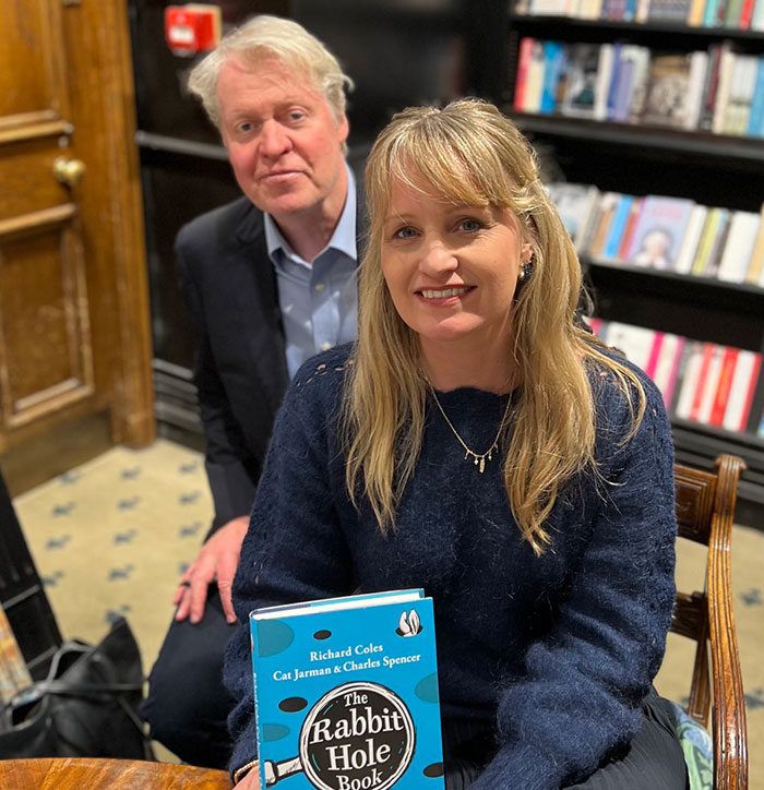 Two people in a bookstore, one holding \"The Rabbit Hole Book\" by Richard Coles, Cat Jarman, Charles Spencer.