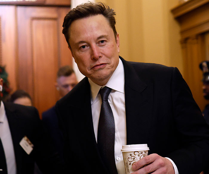 Elon Musk in a suit holding a coffee cup, related to the 20 billion tunnel project for rapid travel.