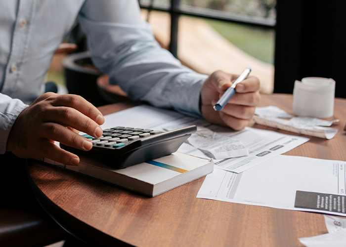 Person uses calculator and pen at a desk with documents, focusing on employer demands and overpayment issues.