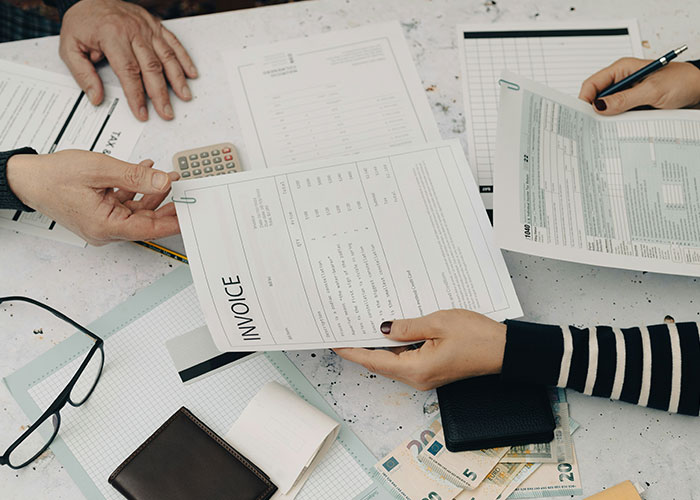 Hands holding invoices and documents over a table with cash and a calculator, illustrating employer demands for overpayment.