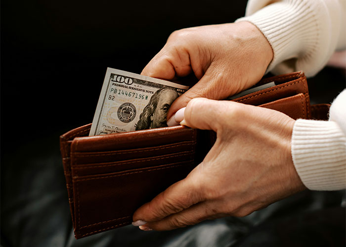 Hands holding a wallet with cash, representing employer demands for overpayment retrieval.