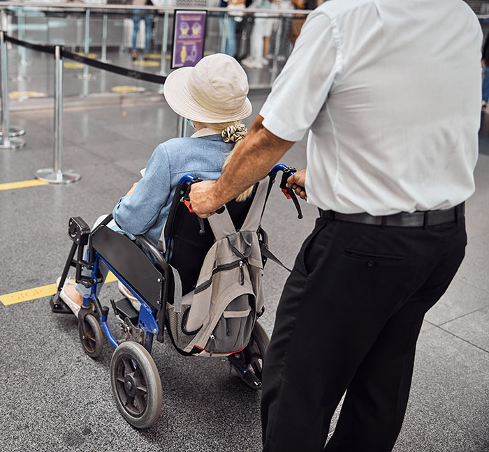 Man pushing woman in a wheelchair at airport, highlighting accessibility issues with passengers in wheelchairs.