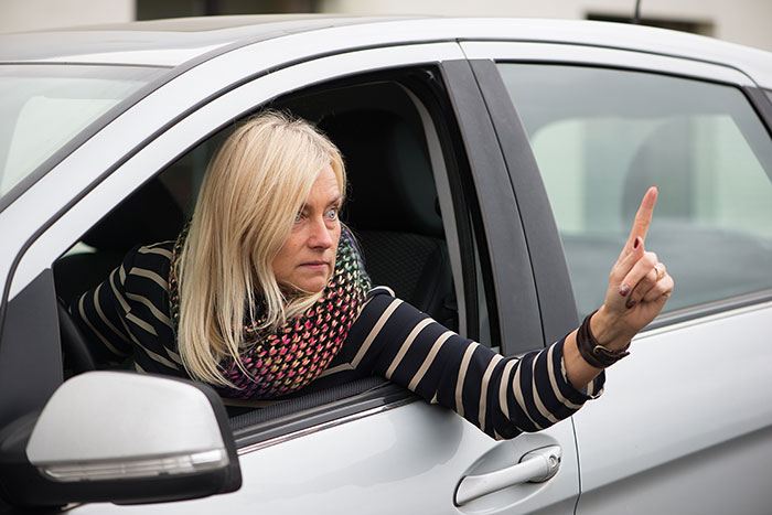 Blonde woman in a car making a gesture, with police presence implied in the scenario, highlighting karma and behavior.