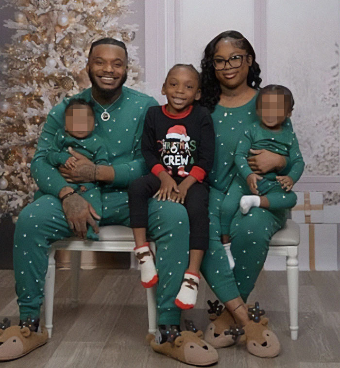 Family in green pajamas with son wearing different Christmas pajamas sitting in front of a decorated tree.