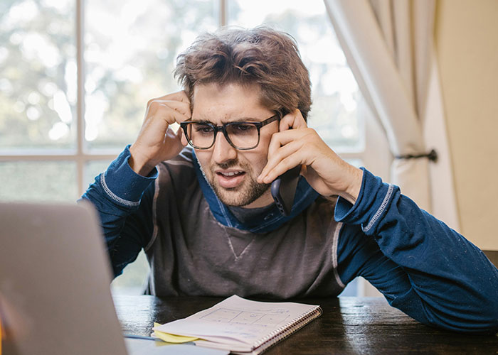 Man looking stressed while talking on the phone, with a notepad and laptop, reflecting CEO management challenges.