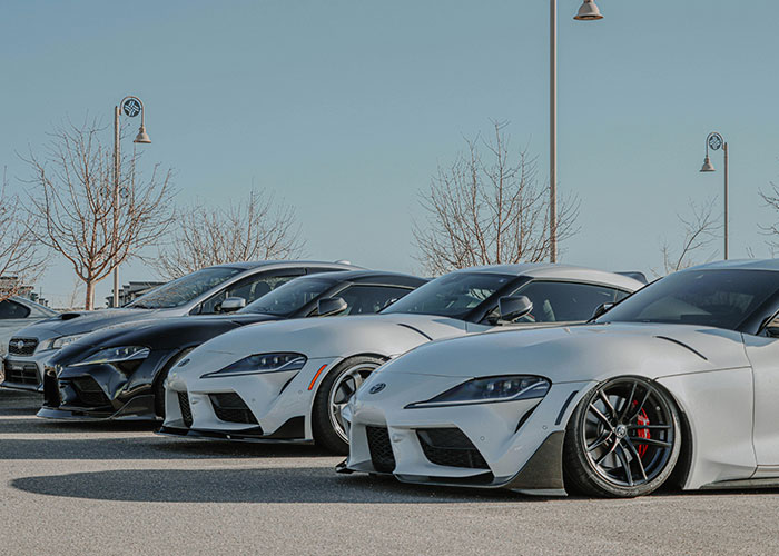 Row of sleek cars parked in an open lot under clear skies, highlighting management decisions in automotive business.