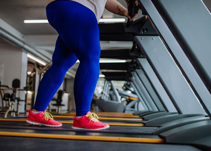 Person in blue leggings on a treadmill at the gym, highlighting fat-shaming issues and fitness.