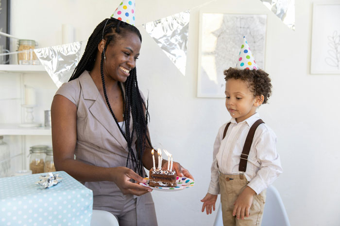 Mother and son at a birthday party with a cake and hats.