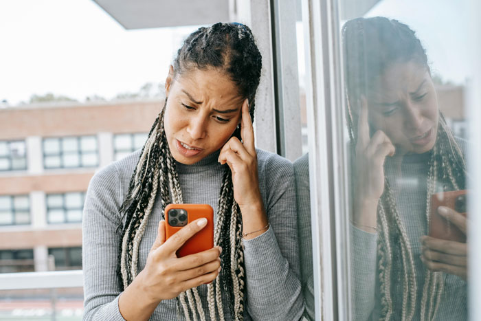 Woman holding a smartphone, looking stressed on a balcony.