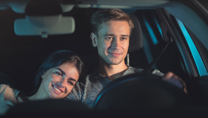 Couple smiling in a car at night, planning a surprise house prank.