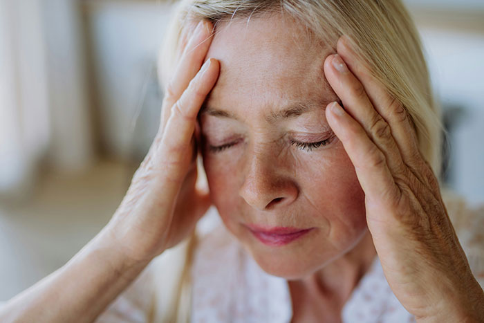 Woman with eyes closed, holding her head, feeling stressed, illustrating spying incident through Gizmo watch.