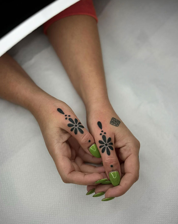 Hands with bold black flower finger tattoos and vibrant green nails.