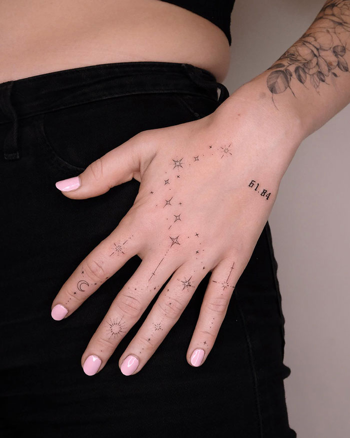 Hand with intricate finger tattoos including stars and numbers, showcasing unique tattoo designs on fingers.